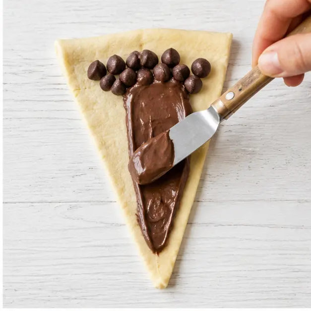 Step 2: spreading room temperature chocolate hazelnut spread over each dough triangle and adding milk chocolate chips