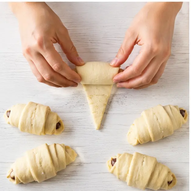 Step 3: rolling each filled triangle from the wide end toward the point and curving the ends into crescent shapes