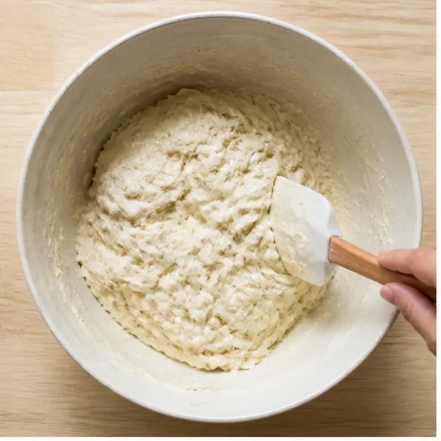 Mixing a sticky shaggy dough in a ceramic bowl with a spatula
