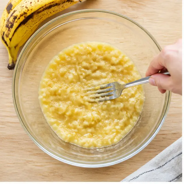 Mashing ripe bananas with a fork in a glass bowl until almost pureed
