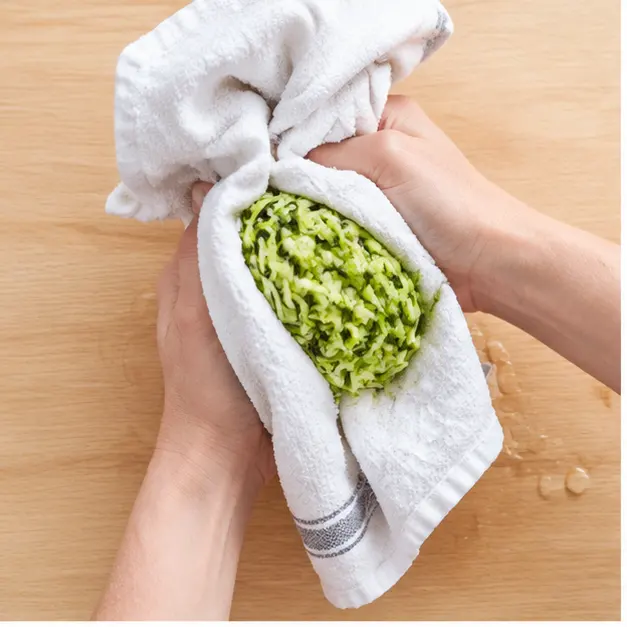 Squeezing shredded zucchini in a dish towel to remove excess moisture