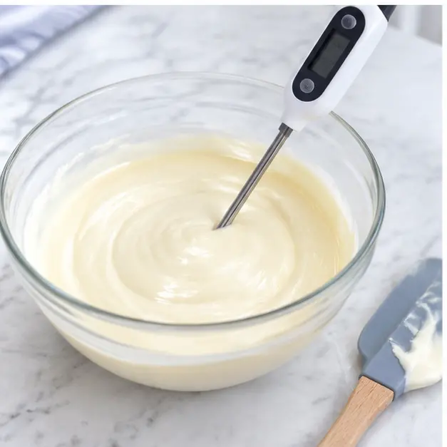 Step 3: Checking the white ganache temperature with a digital instant-read thermometer as it cools toward 85 to 95 degrees and thickens to a slow ribbon